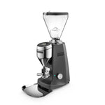 A professional electric coffee grinder with a dark gray body, a clear hopper, and a polished stainless steel bean hopper and base, shown on a solid white background.